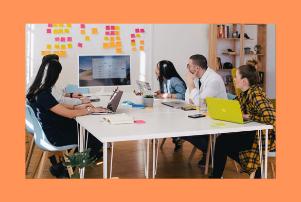 Adults sitting around a table with laptops, pens and notes, looking at a screen on a wall surrounded by colourful post-it notes.
